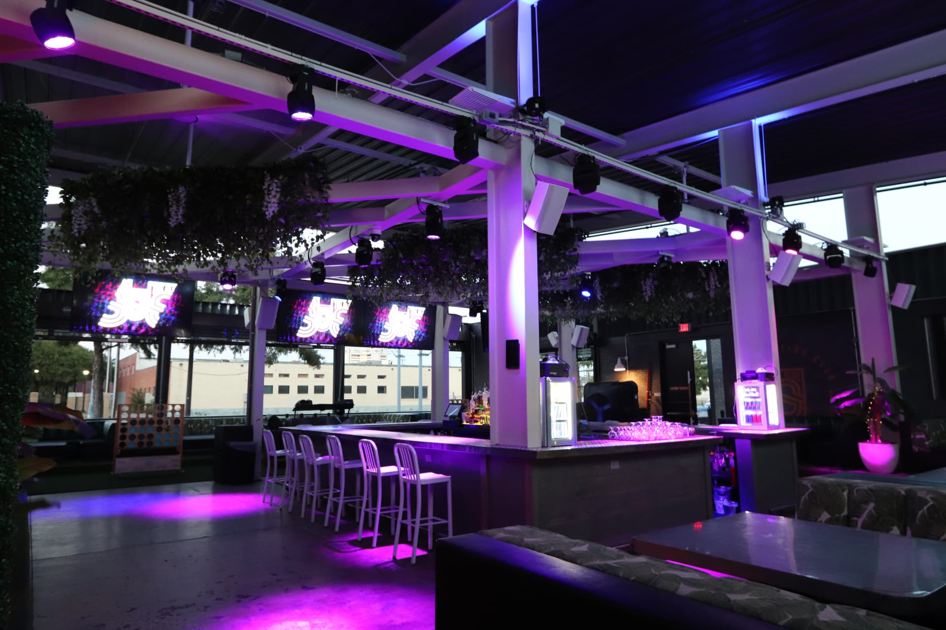 Sporting Club Dallas covered patio lounge with purple neon lighting, bar seating, and sports screens